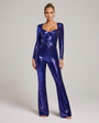 Voorkant van de jumpsuit in paarsblauwe pailletten, model staat recht met armen langs het lichaam en draagt gouden oorringen. 4