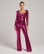 Model in fuchsia roze pailletten jumpsuit, voorkant, staand met armen langs het lichaam, hartvormige halslijn, riem en uitlopende pijpen. 1