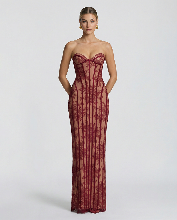 Model draagt de strapless maxi-jurk van bordeauxrode bloemenkant met korsetribben, frontaal gefotografeerd met de handen langs het lichaam. 1