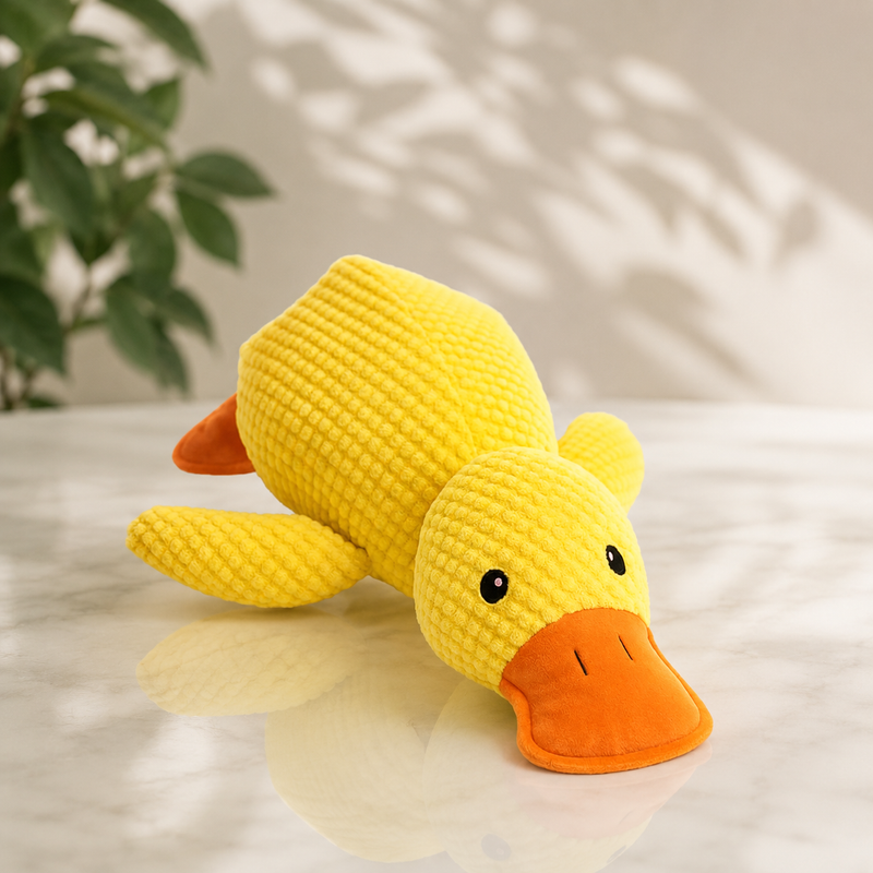 Gele pluchen eend met oranje snavel ligt op een marmeren tafel naast een plant 1