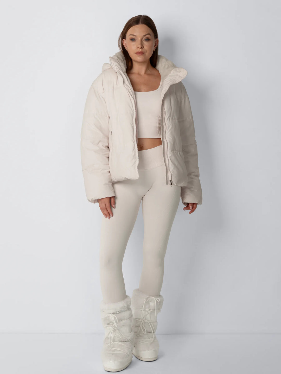Volledig vooraanzicht van model in open crèmekleurige pufferjack met bijpassende legging, crop top en bontlaarzen 5