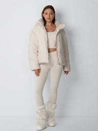 Volledig vooraanzicht van model in open crèmekleurige pufferjack met bijpassende legging, crop top en bontlaarzen 5