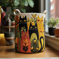 Ronde gewatteerde mand met kleurrijke kattenprint en twee stoffen handgrepen, staand op een houten vloer bij een raam met planten. 1