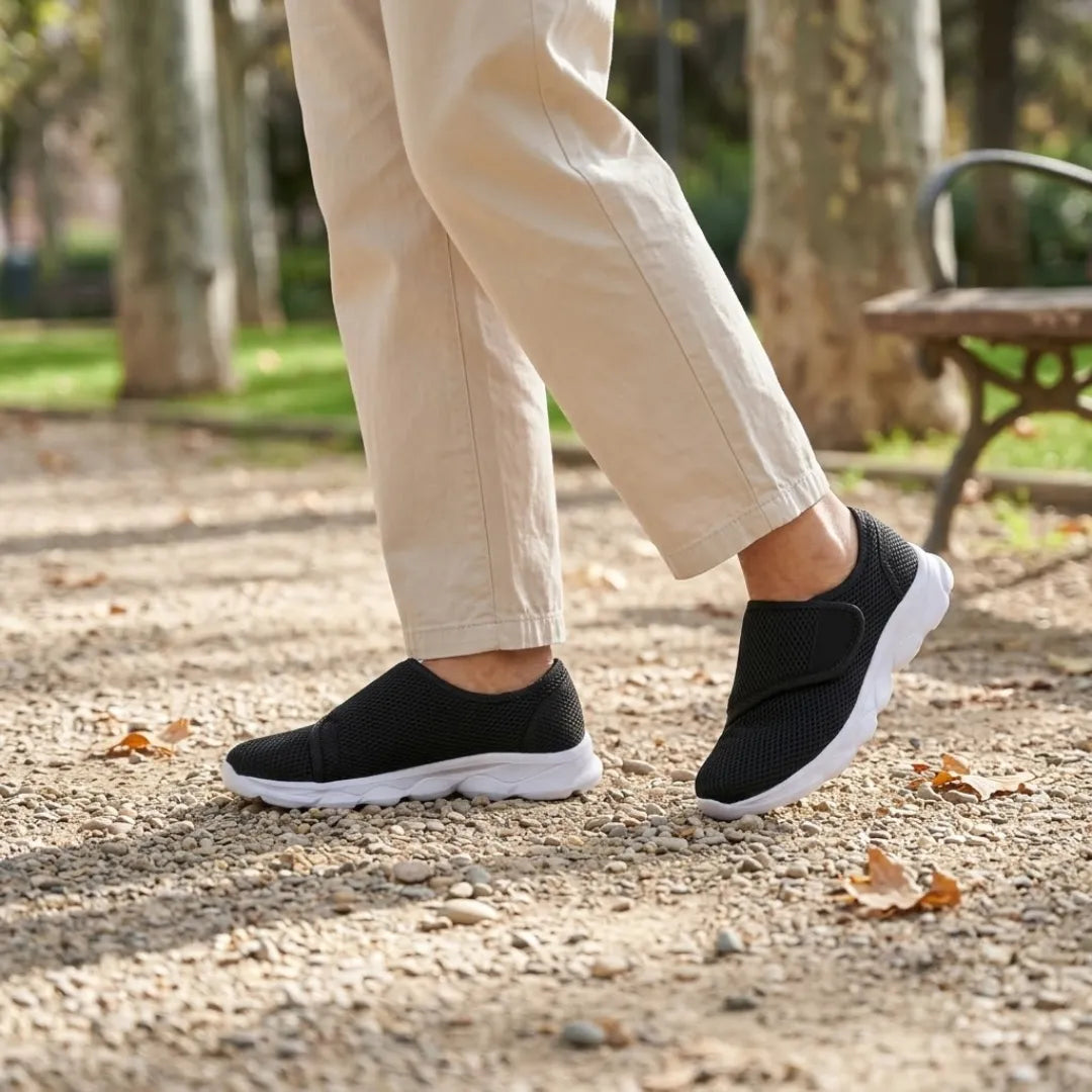 Zwarte mesh schoenen met witte zool en klittenband gedragen tijdens een wandeling op een grindpad bij een parkbankje. 20