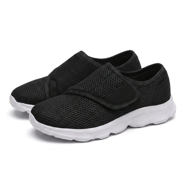 Paar zwarte mesh schoenen met witte zool en klittenbandsluiting, schuin van voren gefotografeerd. 25