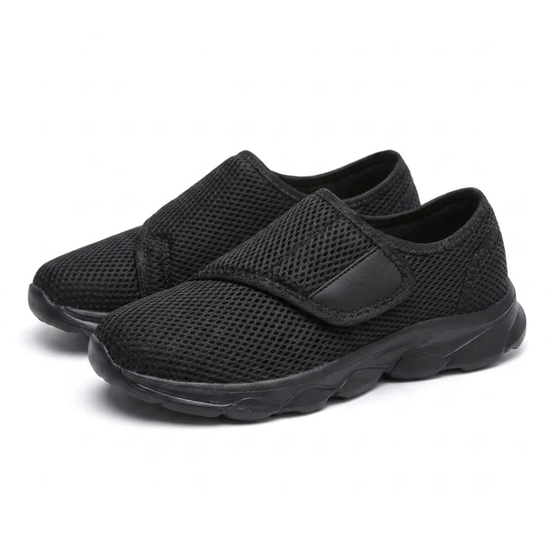 Schuin aanzicht van een paar geheel zwarte mesh schoenen met klittenbandsluiting en zwarte zool. 16