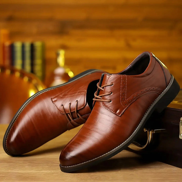 Twee glanzende cognacbruine veterschoenen met brogue-detail, schuin tegen een houten koffer op een houten tafel. 1