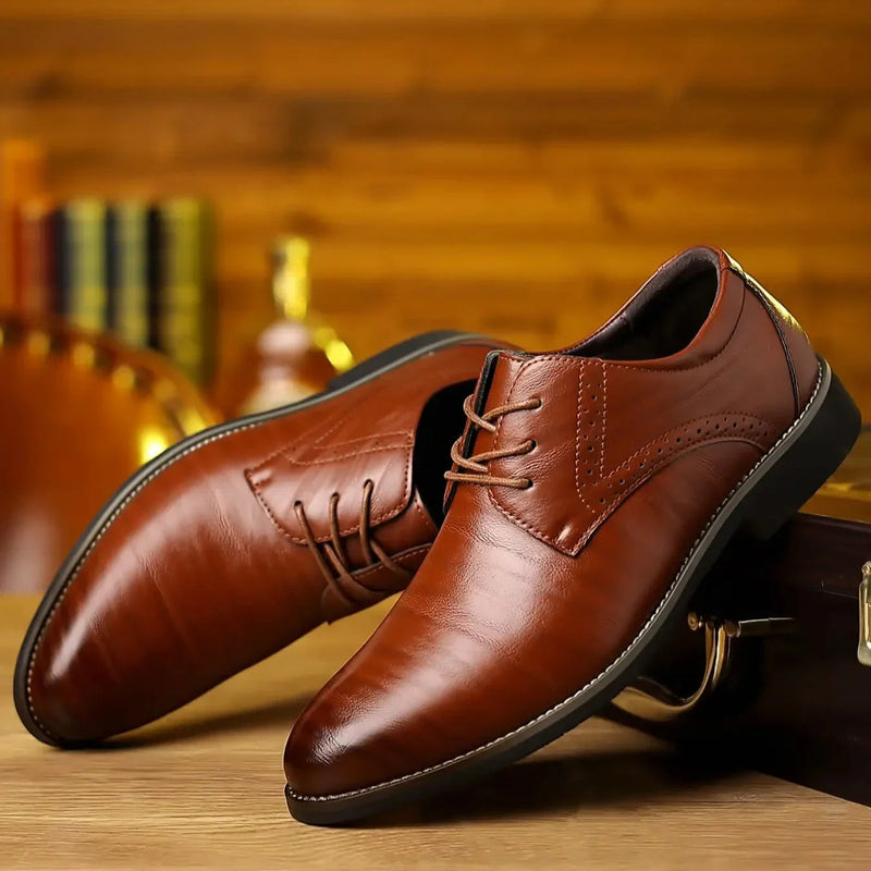 Twee glanzende cognacbruine veterschoenen met brogue-detail, schuin tegen een houten koffer op een houten tafel. 1