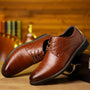 Twee glanzende cognacbruine veterschoenen met brogue-detail, schuin tegen een houten koffer op een houten tafel. 1
