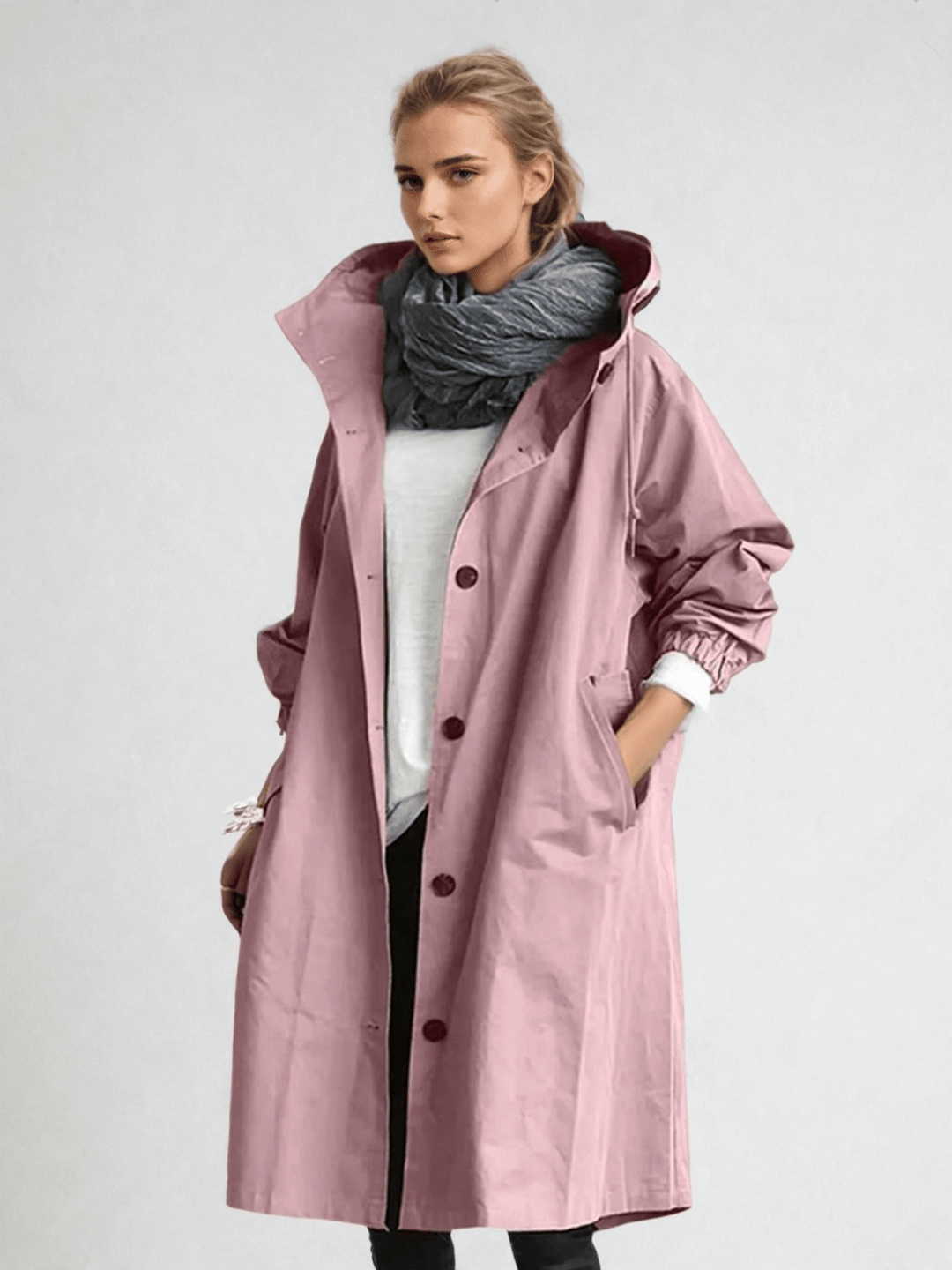 Model draagt de roze trenchcoat met capuchon, elastische manchetten en knoopsluiting over een wit shirt met grijze sjaal. 6