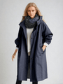 Model draagt de donkerblauwe trenchcoat met grote capuchon en knopen, gecombineerd met een witte trui en donkere sjaal. 7