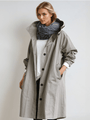 Model draagt de grijze trenchcoat met capuchon open over een wit shirt en donkere sjaal, met een hand in de zak. 1