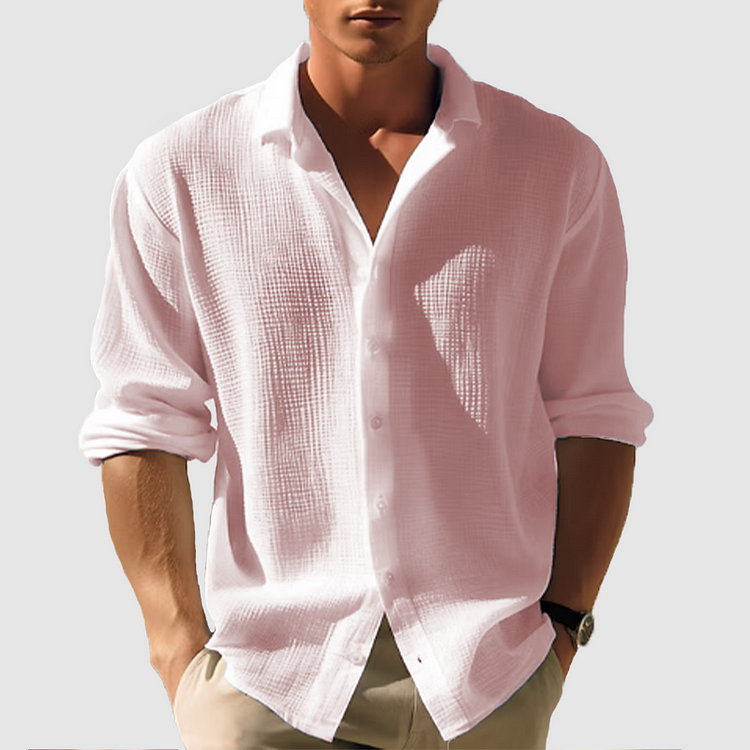 Model draagt het gestructureerde overhemd in zacht roze, met opgerolde mouwen, geopende kraag en een beige broek. 4