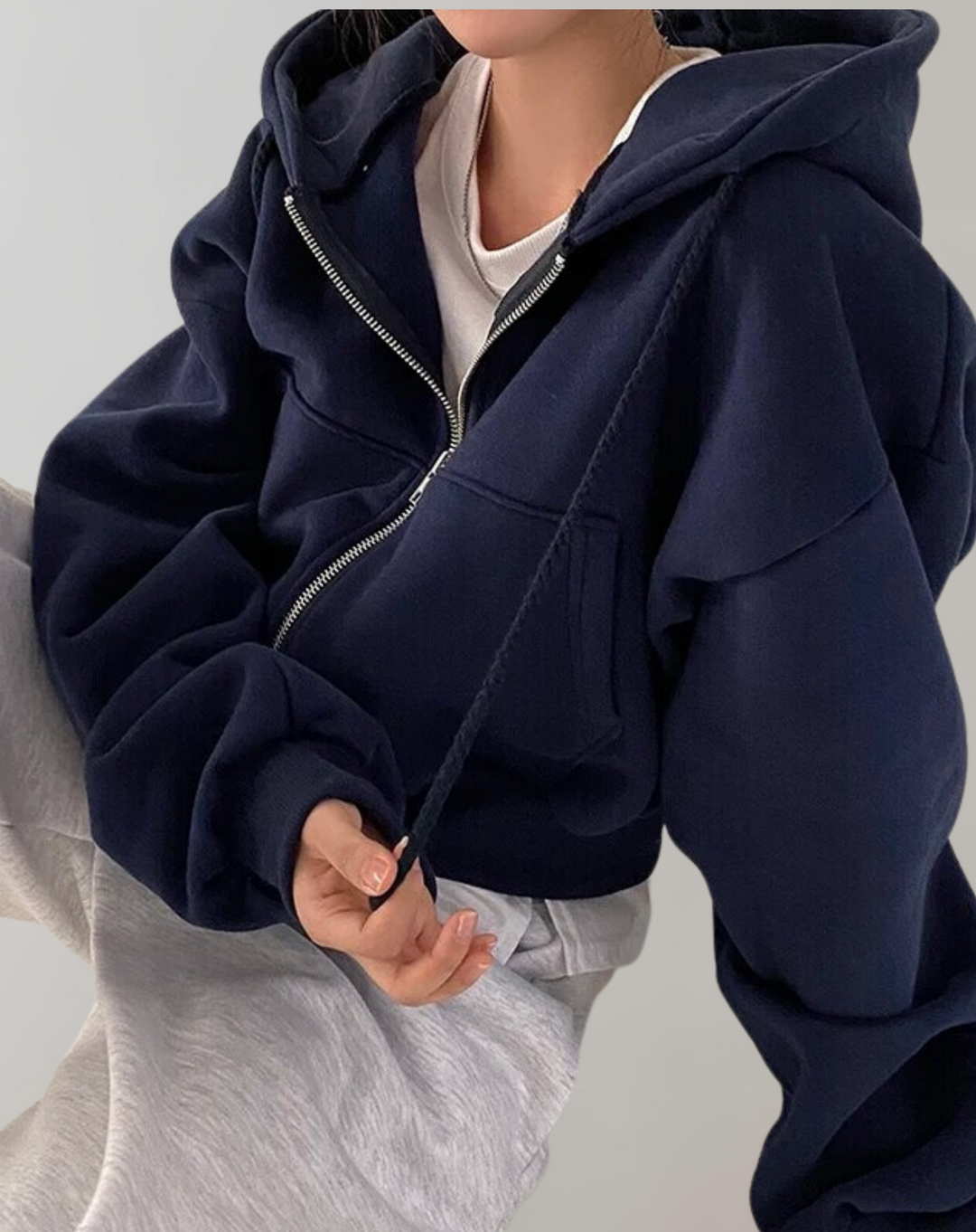 Marineblauwe hoodie met open rits gedragen over een wit topje en een lichtgrijze broek, met een koord dat langs het lijf hangt. 3