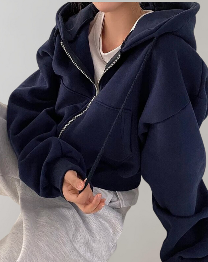 Marineblauwe hoodie met open rits gedragen over een wit topje en een lichtgrijze broek, met een koord dat langs het lijf hangt. 3