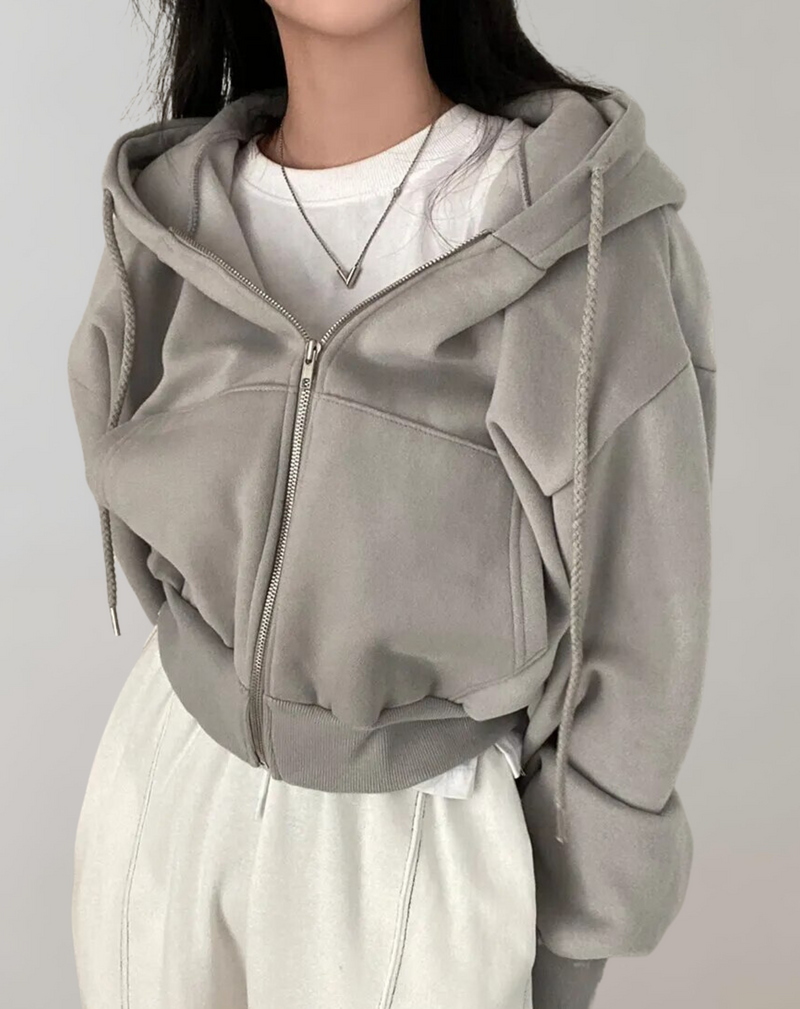 Grijze hoodie gedragen over een wit shirt met ketting, met geribde onderrand, zijzakken en een dichte rits met koorden. 4