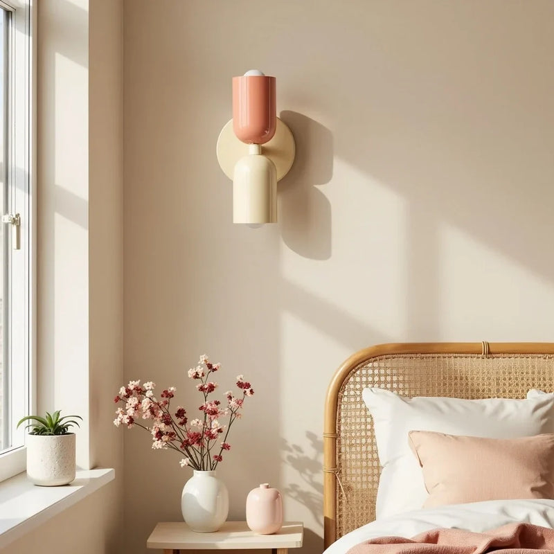 Wandlamp in zalmroze en crème naast een rotan hoofdeinde, met zonlicht dat schaduwen werpt op een beige muur. 2