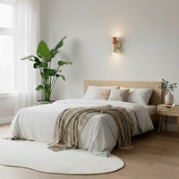 Kleine wandlamp in terracotta en crème boven een bed met wit beddengoed, in een lichte slaapkamer met kamerplant. 8
