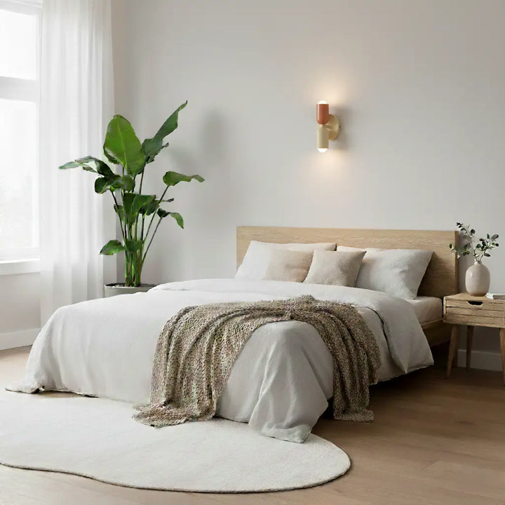 Kleine wandlamp in terracotta en crème boven een bed met wit beddengoed, in een lichte slaapkamer met kamerplant. 8