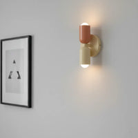 Brandende wandlamp in terracotta en crème met licht naar boven en onder, naast een ingelijste zwart-witprint op een grijze muur. 4