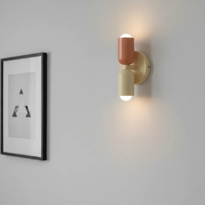 Brandende wandlamp in terracotta en crème met licht naar boven en onder, naast een ingelijste zwart-witprint op een grijze muur. 4