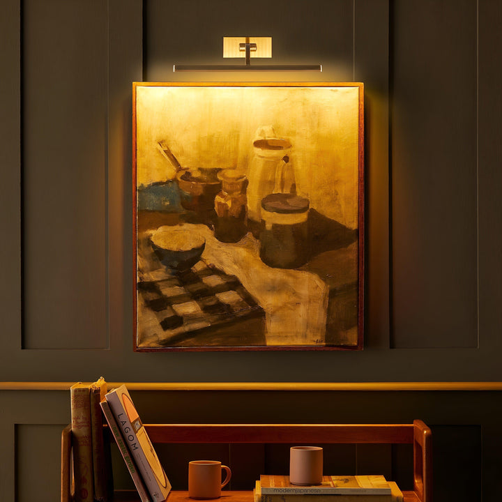 Aanstaande messing schilderijlamp die het ingelijste stilleven in warm goudkleurig licht zet, in een donkere kamer 5