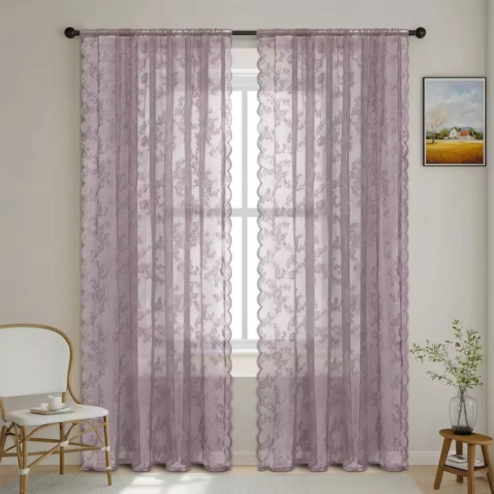 Twee doorzichtige kantgordijnen in een mauve paarsgrijze tint met bloemenpatroon en golvende rand voor een raam in een lichte kamer. 11