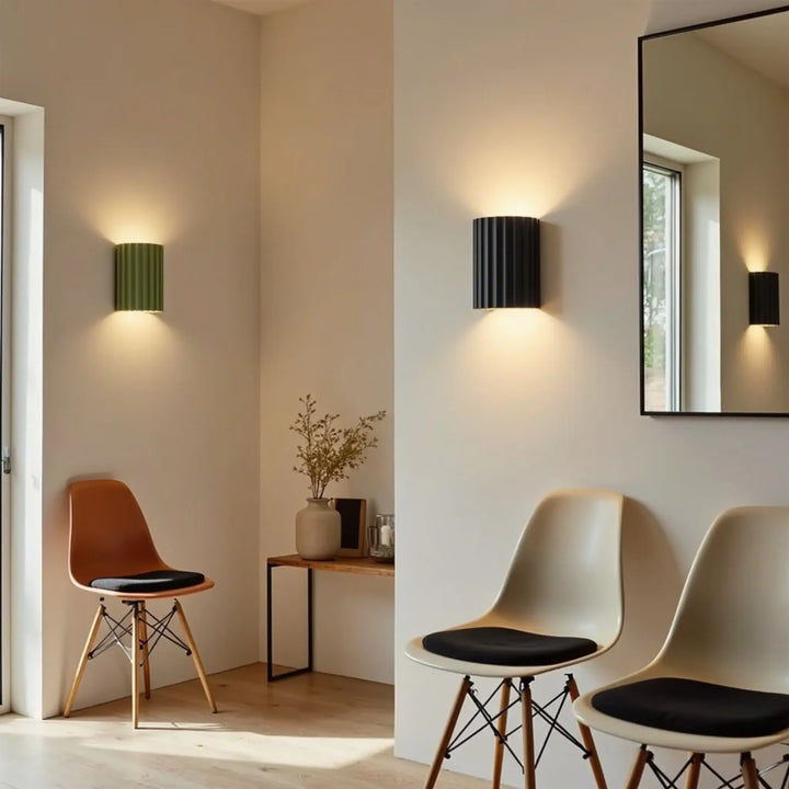 Groene en zwarte geribbelde wandlamp in een lichte hal met stoelen, spiegel en bijzettafel 3