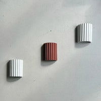 Twee witte en een terracotta geribbelde wandlamp diagonaal op een grijze betonnen muur 13