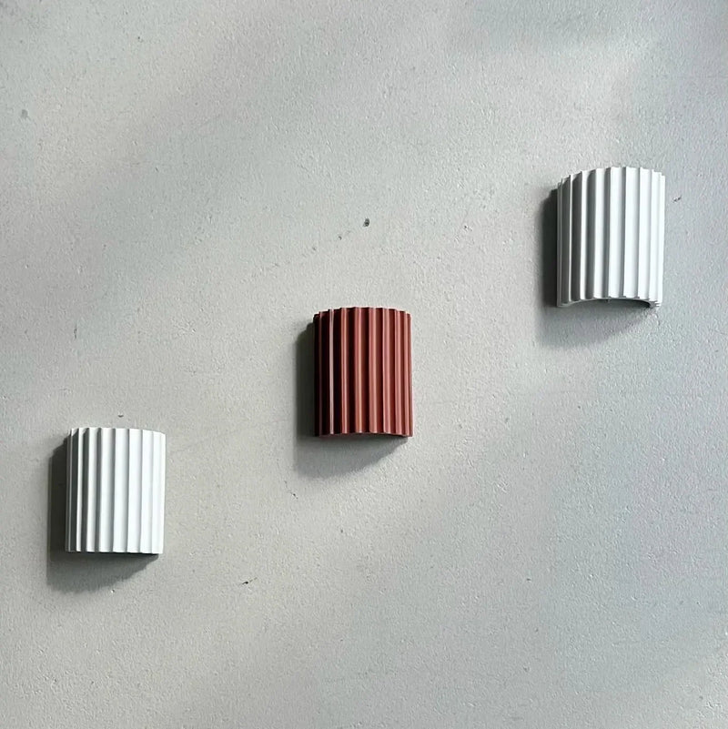 Twee witte en een terracotta geribbelde wandlamp diagonaal op een grijze betonnen muur 13