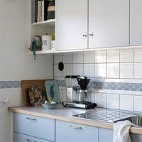 Blauwwitte tegelmotiefstrook op de keukenwand boven een aanrecht met koffiezetapparaat en afdruiprek 16