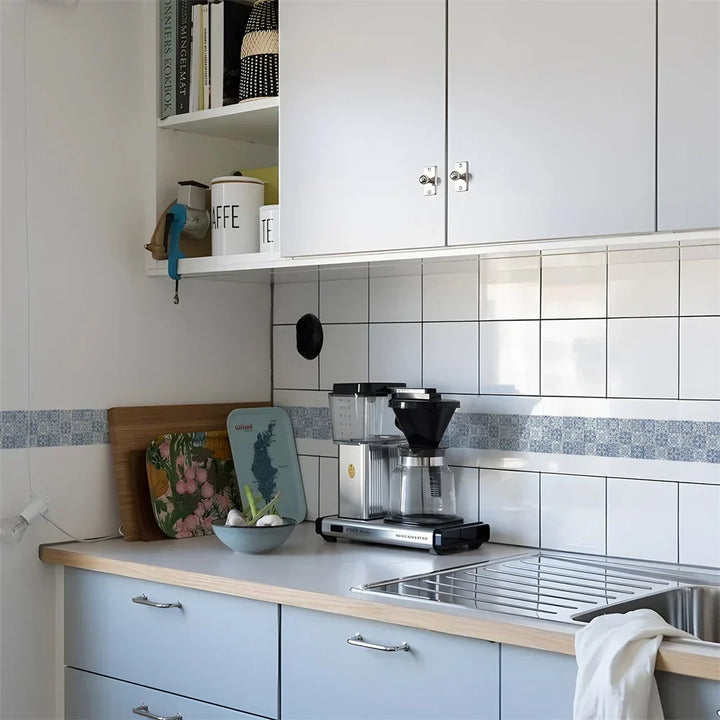 Blauwwitte tegelmotiefstrook op de keukenwand boven een aanrecht met koffiezetapparaat en afdruiprek 16