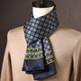Marineblauwe sjaal met vierkante motieven in blauw en geel en een gele randband, gedragen over een beige trui. 22