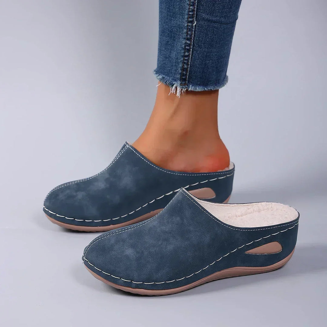 Blauwe pantoffels gedragen met jeans, zijaanzicht waarop de beige fleecevoering aan de binnenkant van de linkerpantoffel te zien is. 4