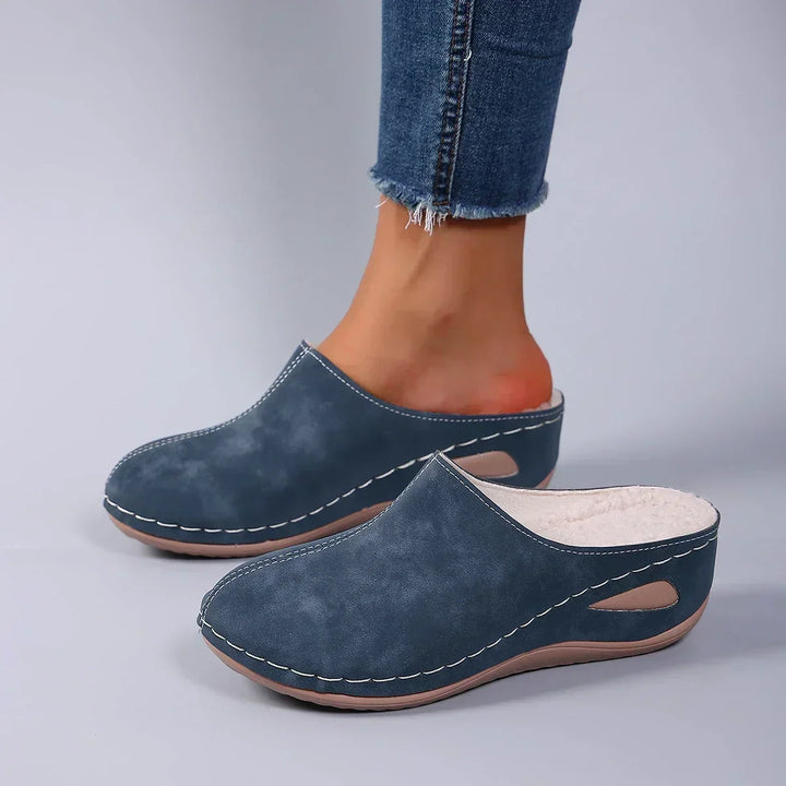 Blauwe pantoffels gedragen met jeans, zijaanzicht waarop de beige fleecevoering aan de binnenkant van de linkerpantoffel te zien is. 4