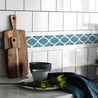Blauwe strook met witte lantaarnvormen tussen witte keukentegels, naast houten snijplanken en servies 64