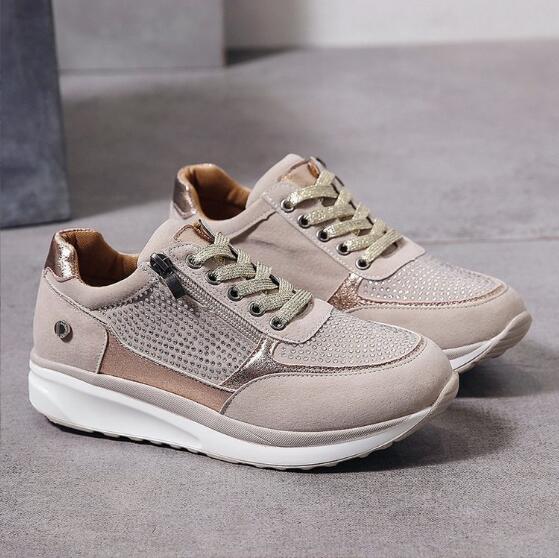 Beige sneakers met goudkleurige veters en steentjes op het bovenwerk, losjes neergezet op een grijze vloer, met zicht op de binnenkant. 2