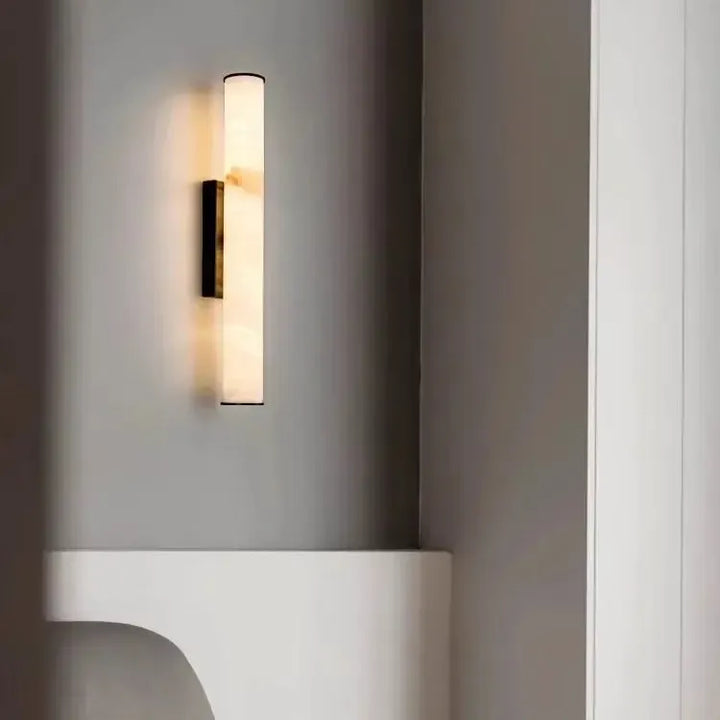 Marmeren wandlamp met donkere afwerking aan een grijze muur boven een witte, gebogen plank naast een witte kolom. 20