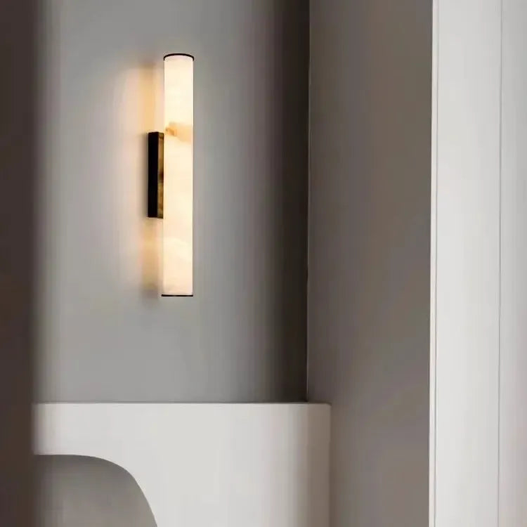 Marmeren wandlamp met donkere afwerking aan een grijze muur boven een witte, gebogen plank naast een witte kolom. 20