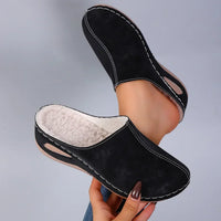 Zwarte pantoffels met de warme fleecevoering goed zichtbaar, een pantoffel in de hand en de andere aan de voet. 5