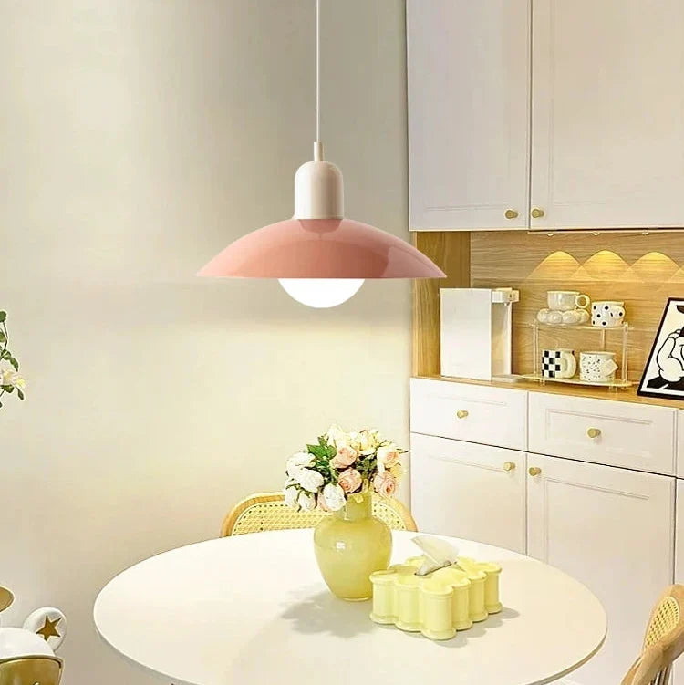 Roze hanglamp met witte fitting boven een ronde tafel en een keukenkast met gouden knoppen 8