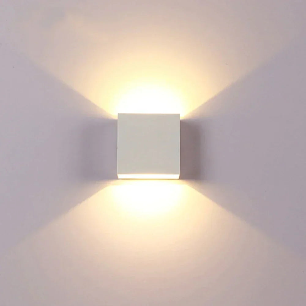Witte kubusvormige wandlamp van voren gezien, met warm licht dat symmetrisch omhoog en omlaag valt op een lichte muur. 17