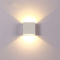 Witte kubusvormige wandlamp van voren gezien, met warm licht dat symmetrisch omhoog en omlaag valt op een lichte muur. 17