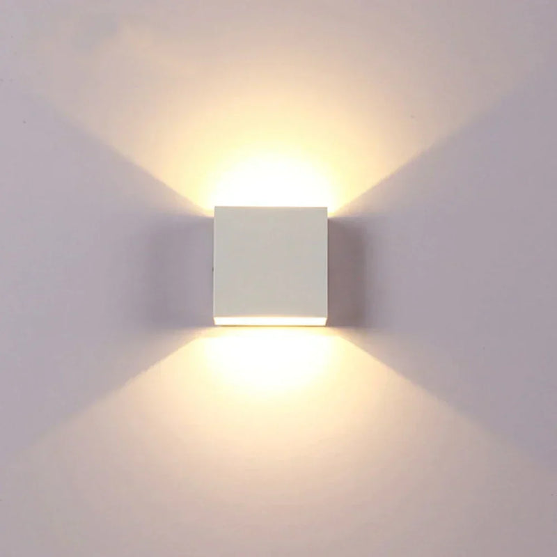 Witte kubusvormige wandlamp van voren gezien, met warm licht dat symmetrisch omhoog en omlaag valt op een lichte muur. 17