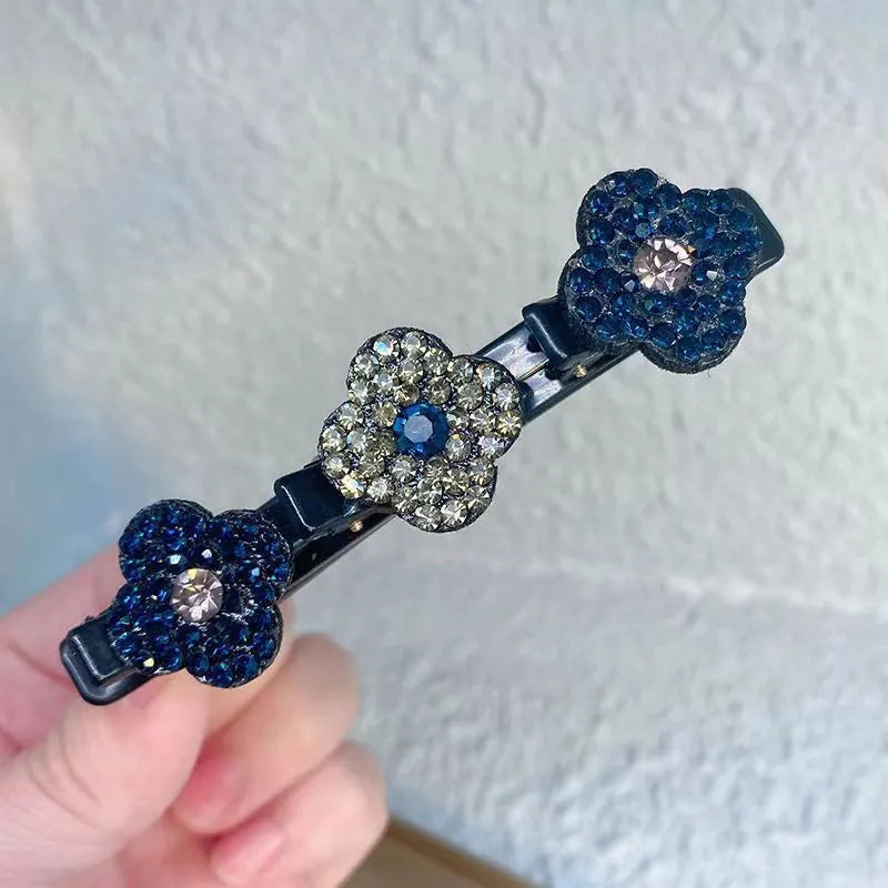 Haarspeld met drie strassbloemen in donkerblauw en grijsgroen met een blauwe steen in het midden, vastgehouden in een hand. 3