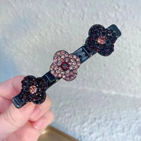 Haarspeld met drie strassbloemen in donkerbordeaux en roze tinten, op een zwarte klem, vastgehouden in een hand. 4