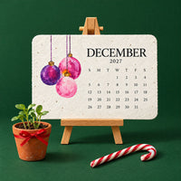 Kalenderkaart december met roze en paarse kerstballen op een ezeltje, naast een potje met kiemplantjes en een zuurstok 3