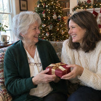 Twee lachende vrouwen op een bank bij de kerstboom geven elkaar een rood ingepakt cadeautje met gouden lint 4