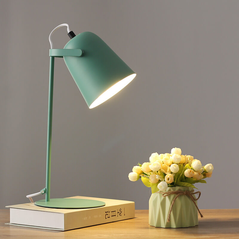 Groene versie van de bureaulamp met brandende kap, op een boek naast een vaasje met roosjes. 9