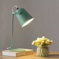 Groene versie van de bureaulamp met brandende kap, op een boek naast een vaasje met roosjes. 9